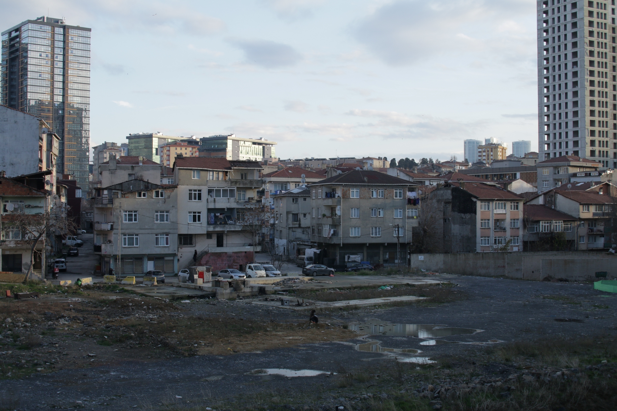 Vue urbaine avec immeubles anciens, terrain vague et buildings modernes en arrière-plan.