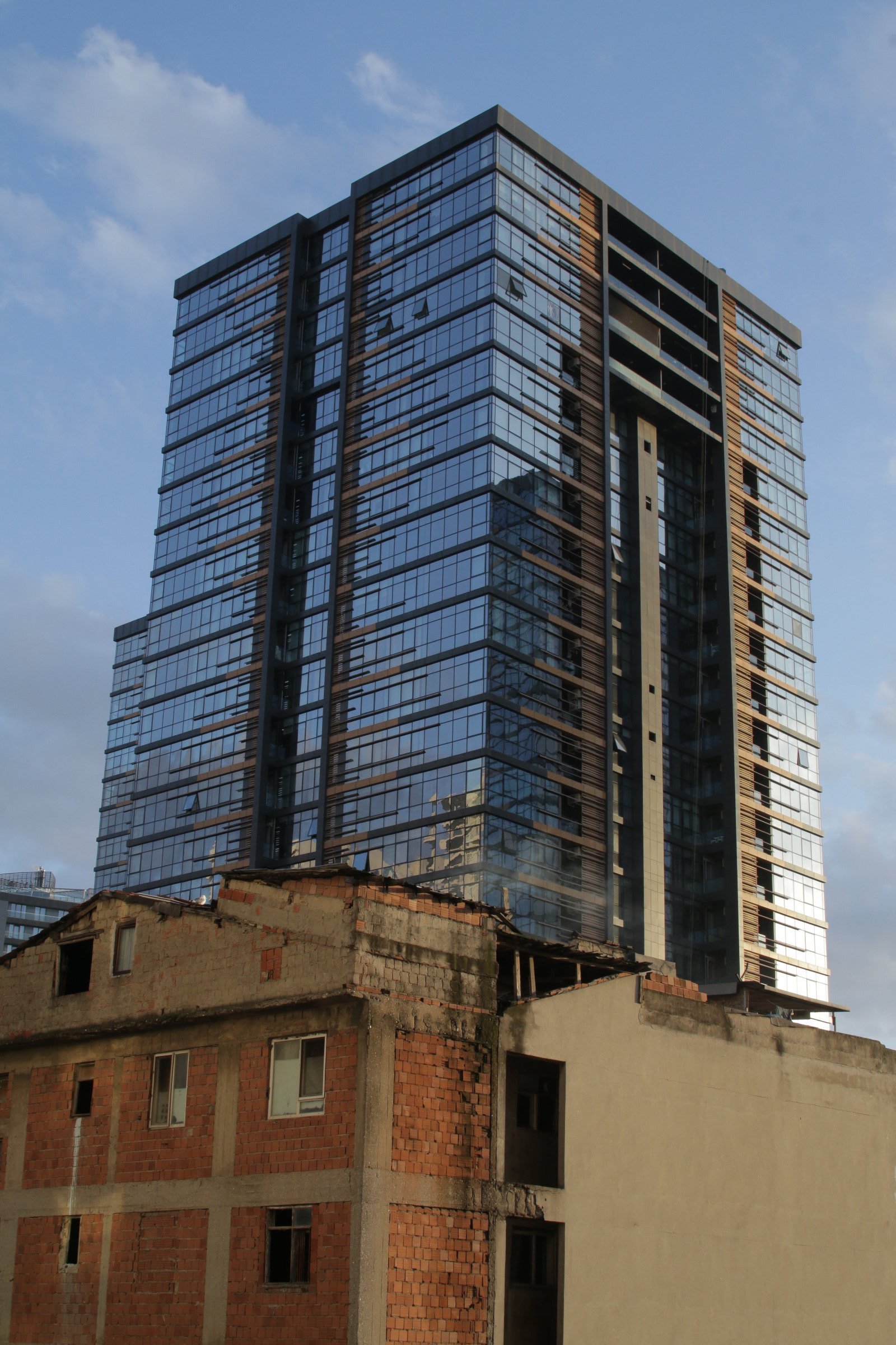 Un immeuble moderne en verre surplombe des bâtiments en briques délabrés.
