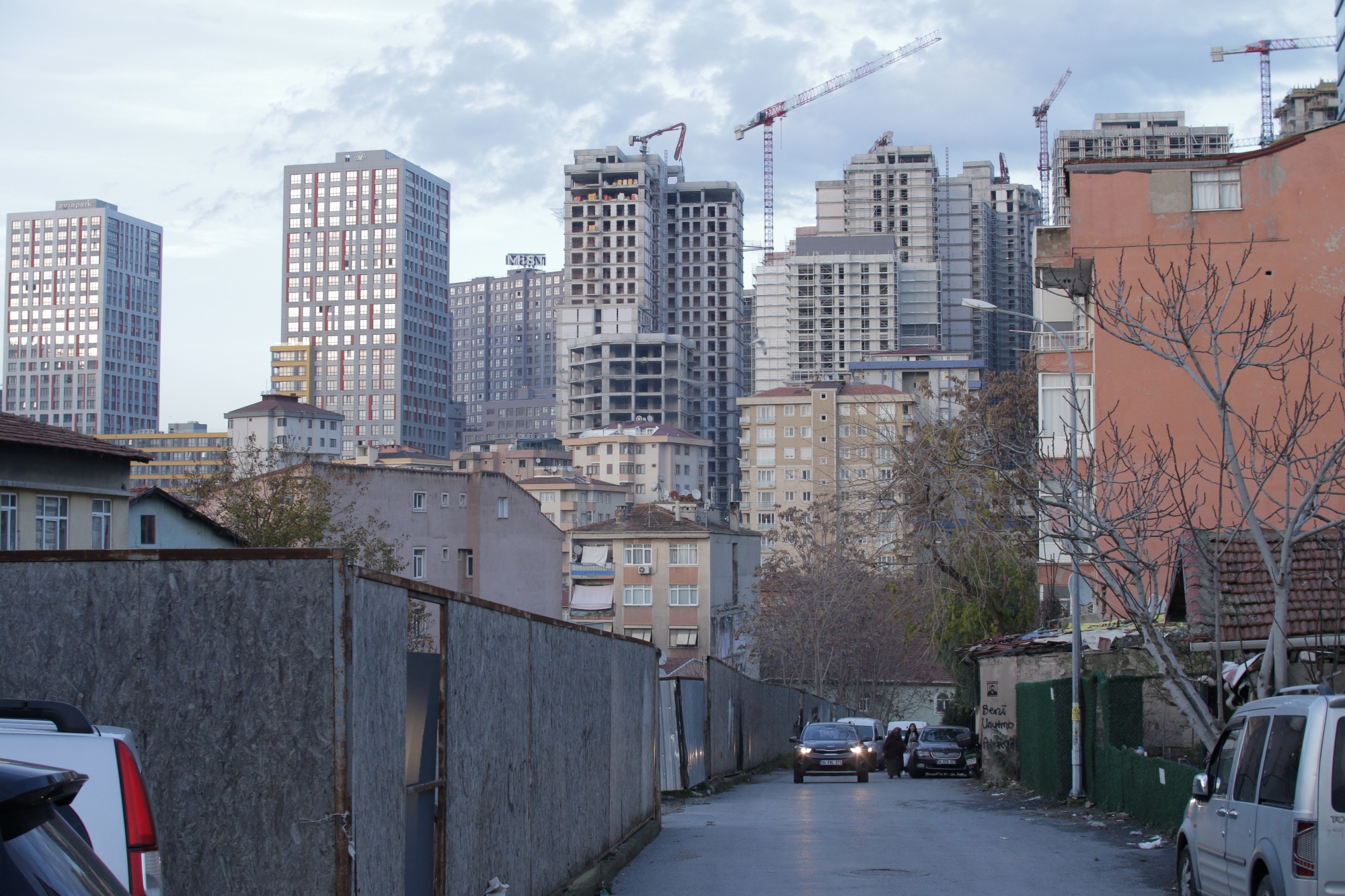 Quartier urbain avec bâtiments en construction et voitures sur une rue étroite.
