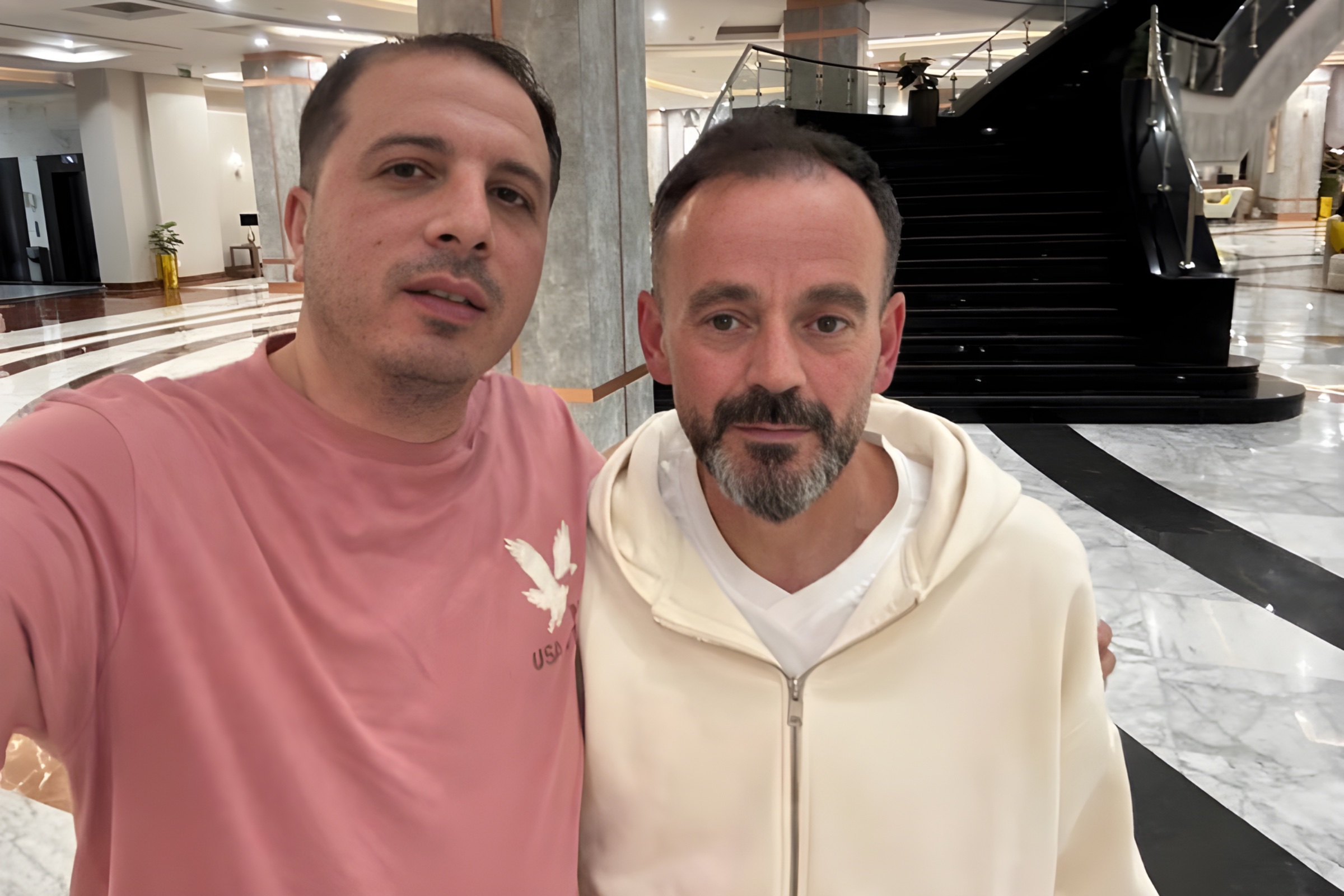 Due uomini sorridenti in un elegante atrio con pavimento lucido e scalinate.