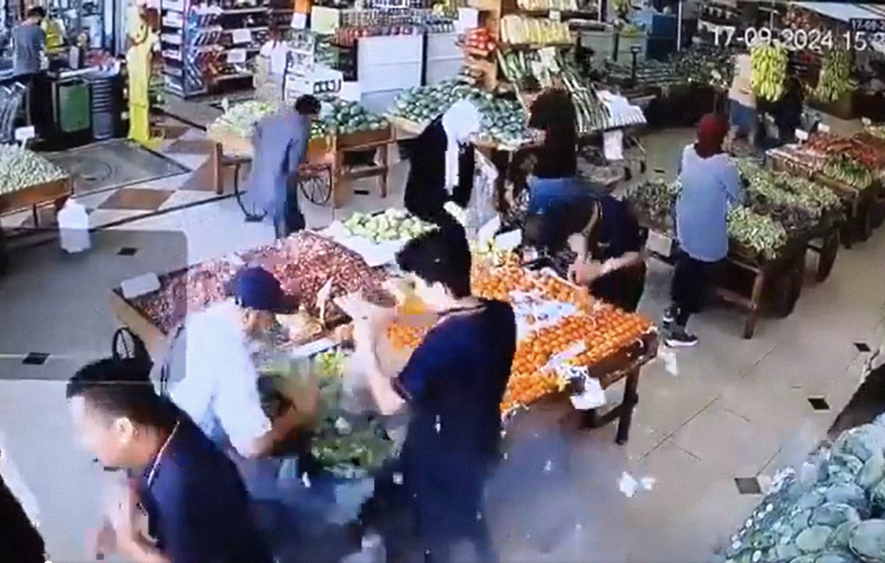 تظهر في الصورة مشهدًا من داخل سوق لبيع الفواكه والخضروات. يبدو أن هناك عددًا من الأشخاص يتواجدون في السوق، حيث يقوم البعض بتفقد المنتجات بينما الآخرون مشغولون بترتيبها أو شراءها. الألوان زاهية، مع الكثير من الفواكه والخضروات المعروضة على الطاولات، مما يعطي انطباعًا بالنشاط والحيوية في المكان. كما أن الإضاءة جيدة، مما يسهل رؤية التفاصيل.