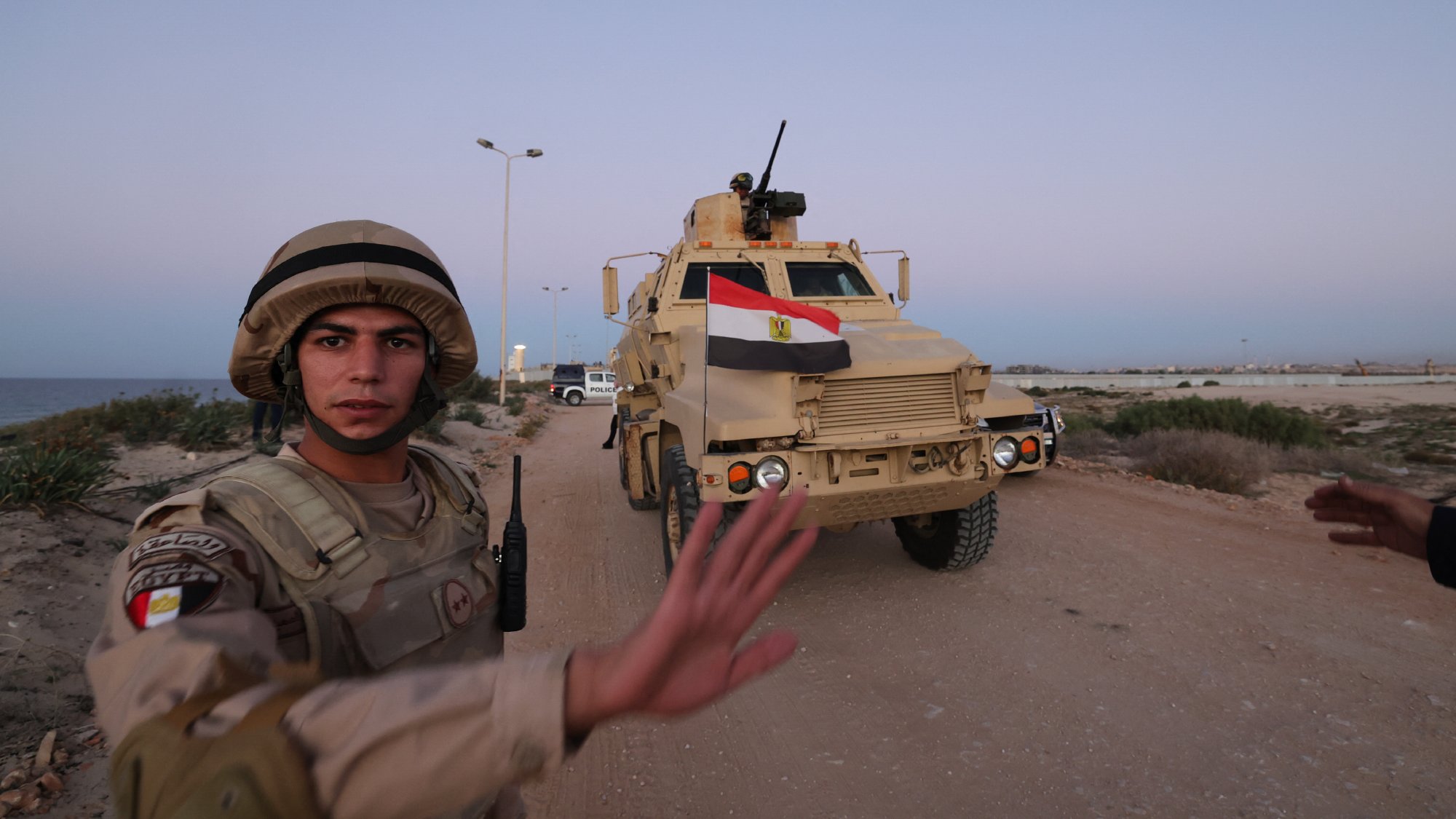 صورة لجندي مصري أمام عربة مدرعة، يظهر العلم المصري وخلفية بحرية.