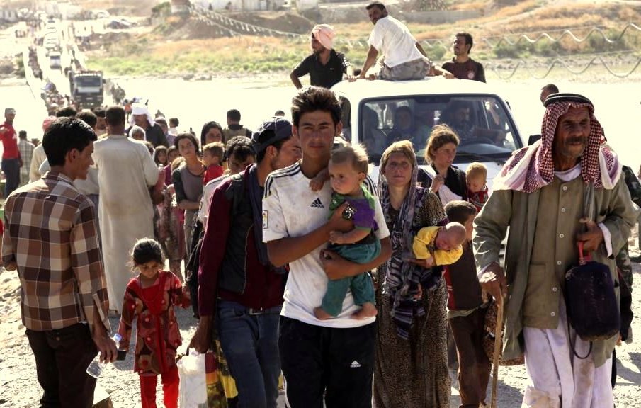 تظهر الصورة مجموعة من الأشخاص الذين يبدون وكأنهم في حالة نزوح. يتواجدون في منطقة مفتوحة، حيث يمشي البعض على الطريق بينما يقف آخرون بالقرب من سيارات. هناك أطفال يحملهم بعض البالغين، مما يعكس معاناة وتحديات العائلات في ظل ظروف صعبة. تُظهر الصورة أيضاً تنوعاً في الأعمار والملابس، مما يدل على أن هؤلاء الأشخاص قد يأتون من خلفيات مختلفة. الأجواء تبدو حزينة وتعبر عن الشعور بالفقد والبحث عن الأمان.