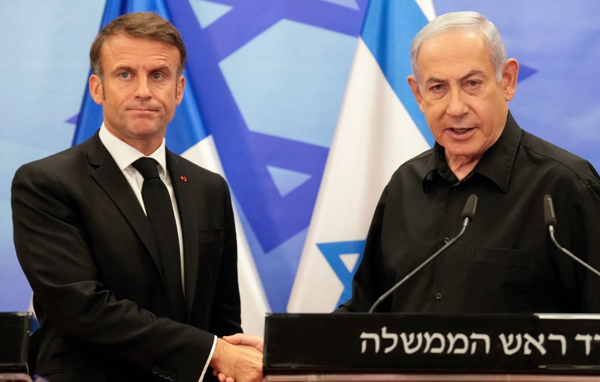 تظهر الصورة اثنين من الرجال أثناء مصافحة، حيث يقف أحدهما على اليمين وهو يرتدي ملابس سوداء، بينما الآخر يرتدي بدلة سوداء طويلة الأكمام. خلفهم تظهر أعلام، يبدو أنها تعود لدولة إسرائيل. تدل تعابير وجوههم على جدية اللقاء، ومن الواضح أنه حدث رسمي.