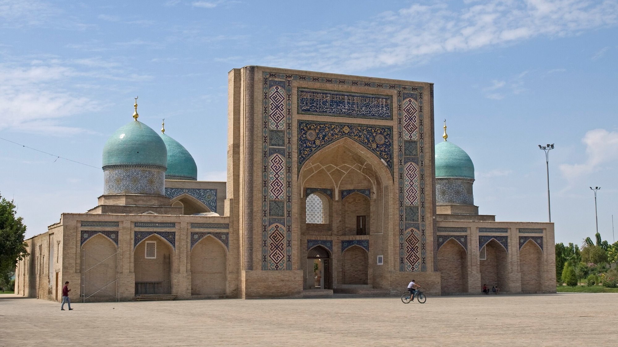 تظهر الصورة معمارًا تاريخيًا بأقواس وقباب زرقاء في سماء صافية. جو مريح.