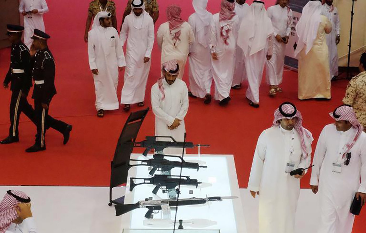 تظهر في الصورة مجموعة من الرجال العرب يرتدون الأزياء التقليدية، يتجولون في مكان يظهر فيه عرض للأسلحة. في وسط الصورة، توجد حاوية زجاجية تحتوي على عدة أنواع من الأسلحة، بما في ذلك البنادق. في الخلفية، يظهر بعض الأفراد المناسبين، مما يوحي بأن الحدث قد يكون معروضًا أو معرضًا للأسلحة أو الأمن. الأجواء تبدو رسمية وجادة، مع وجود السجادة الحمراء في الأرضية.