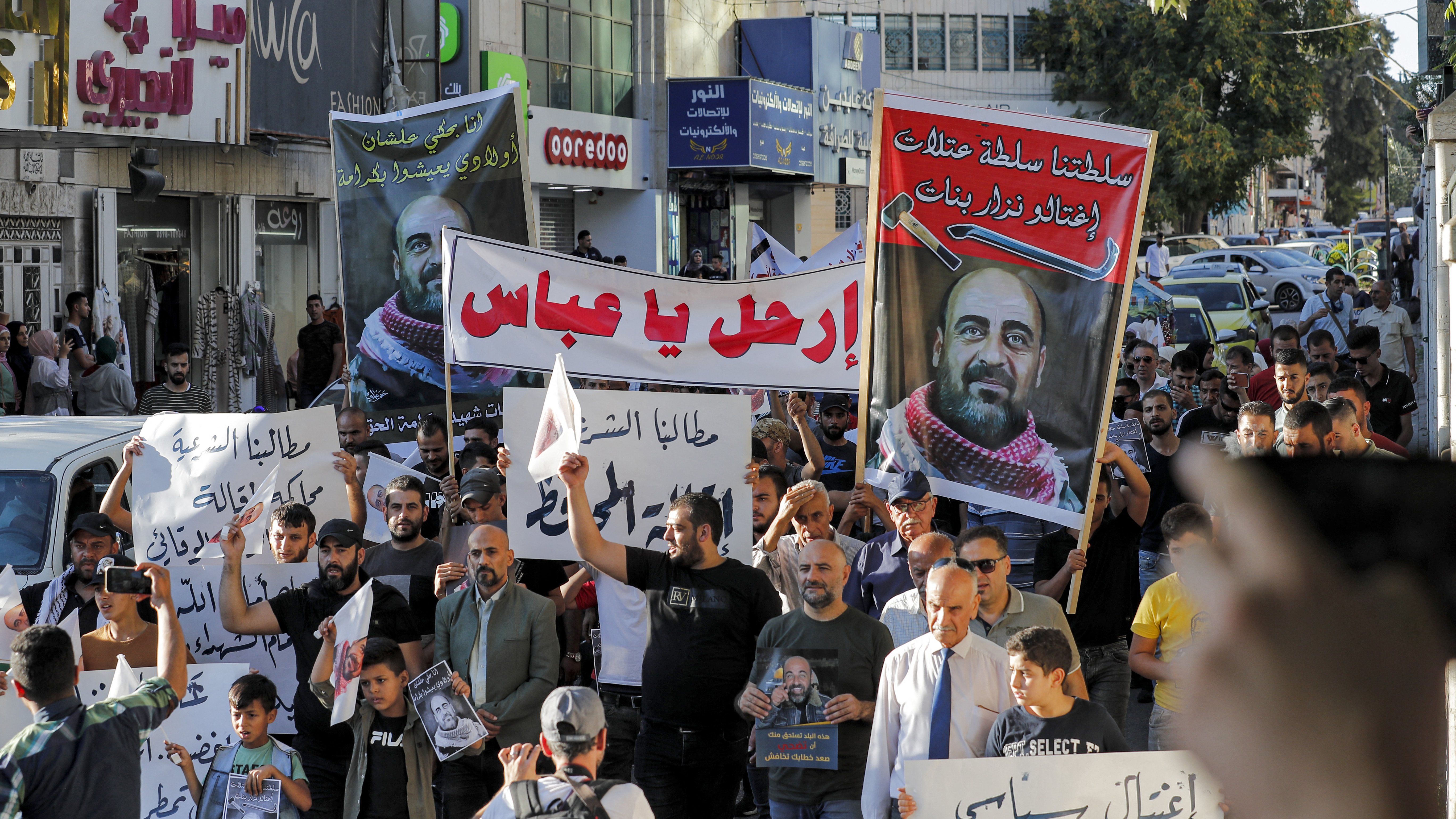 الصورة تُظهر مجموعة من المتظاهرين في شارع يجمعهم الاحتجاج، حيث يحملون لافتات كبيرة تحمل شعارات ومطالب تعبر عن قضايا معينة. يظهر في الصورة عدد من الرجال والنساء والأطفال، وبعضهم يرتدي القمصان بتصاميم مختلفة. يبدو الحشد نشطاً ومتفاعلاً، واللافتات مكتوبة باللغة العربية، مما يدل على أن التظاهر يتناول قضايا محلية. الجو يبدو حماسياً مع وجود بعض السيارات في الخلفية.