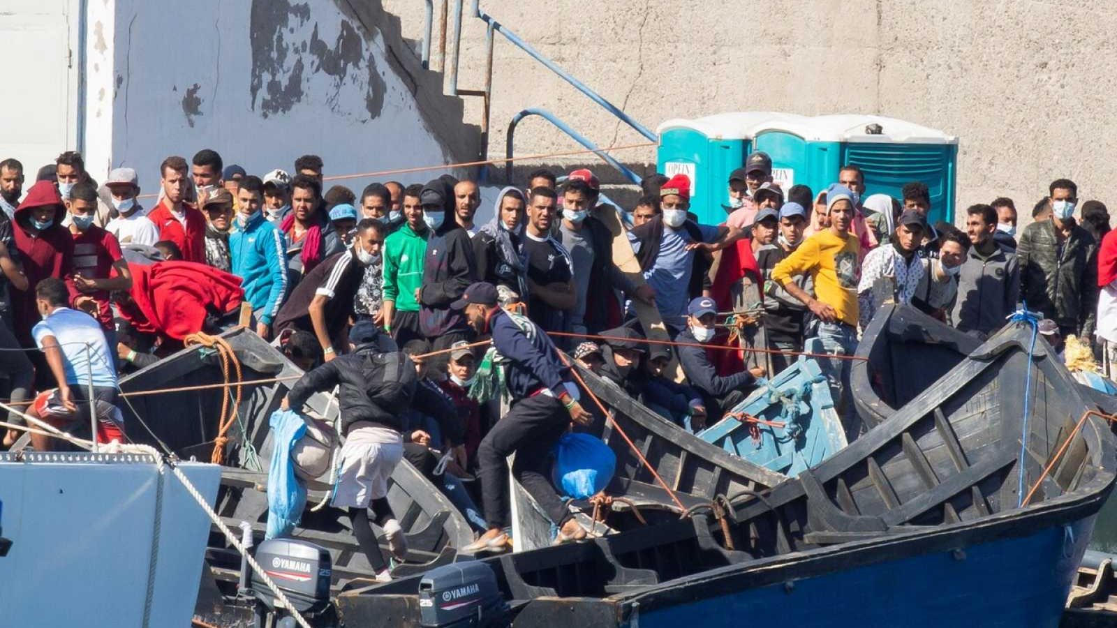 تظهر الصورة مجموعة من الناس يجتمعون حول قوارب في منطقة ميناء أو ساحل. يبدو أن هناك العديد من الأشخاص يتواجدون على القوارب، وبعضهم في وضعية استعداد للانطلاق. يرتدي البعض كمامات أو ملابس متنوعة، وهناك تجمع كبير من الناس يظهرون على جانب الميناء. الأجواء تعكس حالة من الحركة والنشاط، وربما تشير إلى عملية نقل أو هجرة.