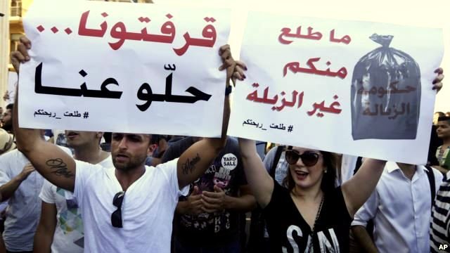 L'image montre une manifestation où des personnes tiennent des pancartes. Les messages sur les pancartes évoquent des revendications concernant la situation dans leur pays. L'une des pancartes semble exprimer un mécontentement face à la gestion des déchets, tandis que l'autre parle d'un désir de changement ou d'amélioration. Les manifestants semblent passionnés et engagés dans leur lutte. L'ambiance générale suggère une mobilisation citoyenne.