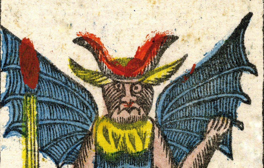 الصورة تظهر كائنًا خياليًا له مظهر يشبه الشيطان أو الوحش. يمتلك أجنحة كبيرة تشبه أجنحة الخفافيش، ومخالب، ومظهرًا جسديًا يجمع بين الصفات البشرية والحيوانية. يرتدي الكائن ملابس ملونة، حيث يظهر بجسم عارٍ مع تفاصيل على الصدر، ورأسه مزين بقرون. في يده يحمل عصا، مما يضفي على الصورة جواً من الغموض والرعب. الألوان المستخدمة في الصورة زاهية وتساعد في تعزيز مظهر الكائن الخيالي.