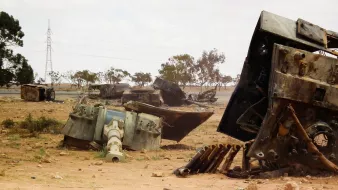 تظهر في الصورة مجموعة من الآليات العسكرية المدمرة والمستخرجة في منطقة صحراوية. تتناثر بقايا الدبابات والمعدات في بيئة جافة، مع بعض الأشجار القليلة في الخلفية. السماء ملبدة بالغيوم، مما يعطي إحساسًا بالوحدة والخراب للمكان. الكهربائية متواجدة في الخلفية، مما يشير إلى وجود بنية تحتية قريبة، ولكنها تبدو بعيدة عن هذه الفوضى.