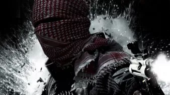 تظهر في الصورة شخصية ملثمة ترتدي غطاء رأس تقليدي، وتحمل أسلحة في يديها. الخلفية تبدو مشوشة وكأنها تعبر عن حالة من الفوضى أو الصراع. كما يظهر جزء من نص عربي في أسفل الصورة، يضيف طابعًا دراميًا للمشهد. تعكس الصورة أجواء من القوة والتوتر.