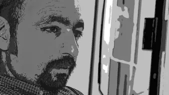 الصورة تظهر رجلًا يبدو في حالة تفكير عميق. ملامحه تُظهر تركيزًا وتأملًا، وهو يرتدي قميصًا مزخرفًا. الإضاءة تنعكس على وجهه، مما يبرز تفاصيله. الخلفية تبدو غير واضحة، مما يعزز من التركيز على العواطف والتعبيرات على وجهه.