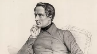 تظهر الصورة شخصية جالسة على كرسي مريح، يبدو أنها لشخصية تاريخية أو فنية. يرتدي ملابس رسمية تضم سترة بأزرار، ويبدو في حالة تأمل أو تفكير. يده تستند إلى فمه، مما يعطي انطباعًا عن عمق تفكيره. الخلفية بسيطة، مما يركز الانتباه على ملامح الشخصية وحالتها التعبيرية.