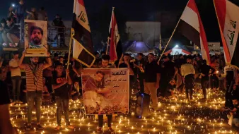 توضح الصورة تجمعًا حاشدًا للناس في مكان مفتوح خلال الليل، حيث يضيء المكان بكثرة الشموع الموزعة على الأرض. يحمل المشاركون لافتات وصورًا، وبعضهم يرفع أعلامًا تمثل بلدانهم. الجو يبدو مهيبًا، حيث يعبر الناس عن حزنهم أو إحياء ذكرى معينة، مما يعكس شعورًا بالوحدة والتضامن في هذه اللحظة.