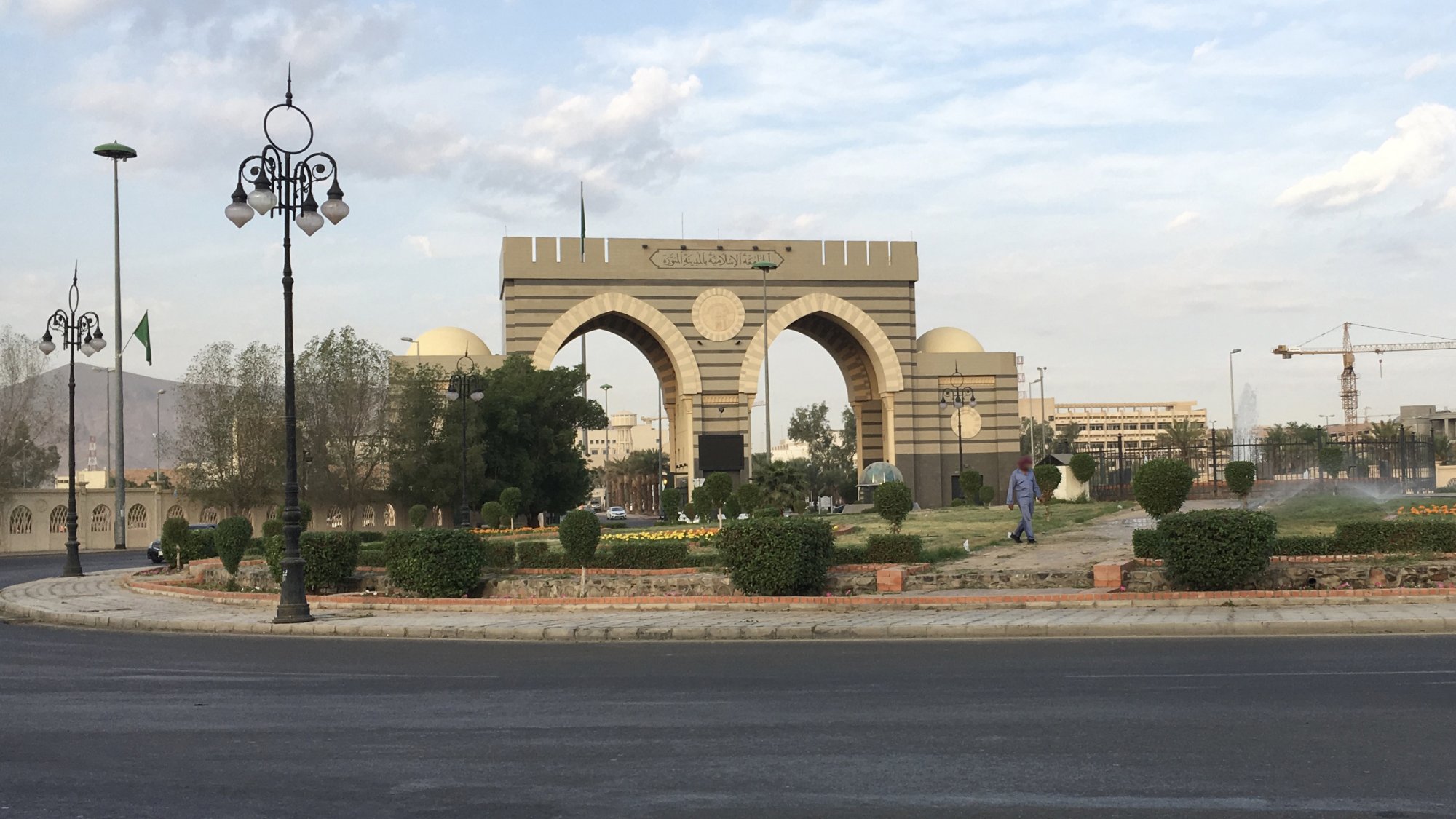 A large archway with decorative towers, surrounded by greenery and a road.