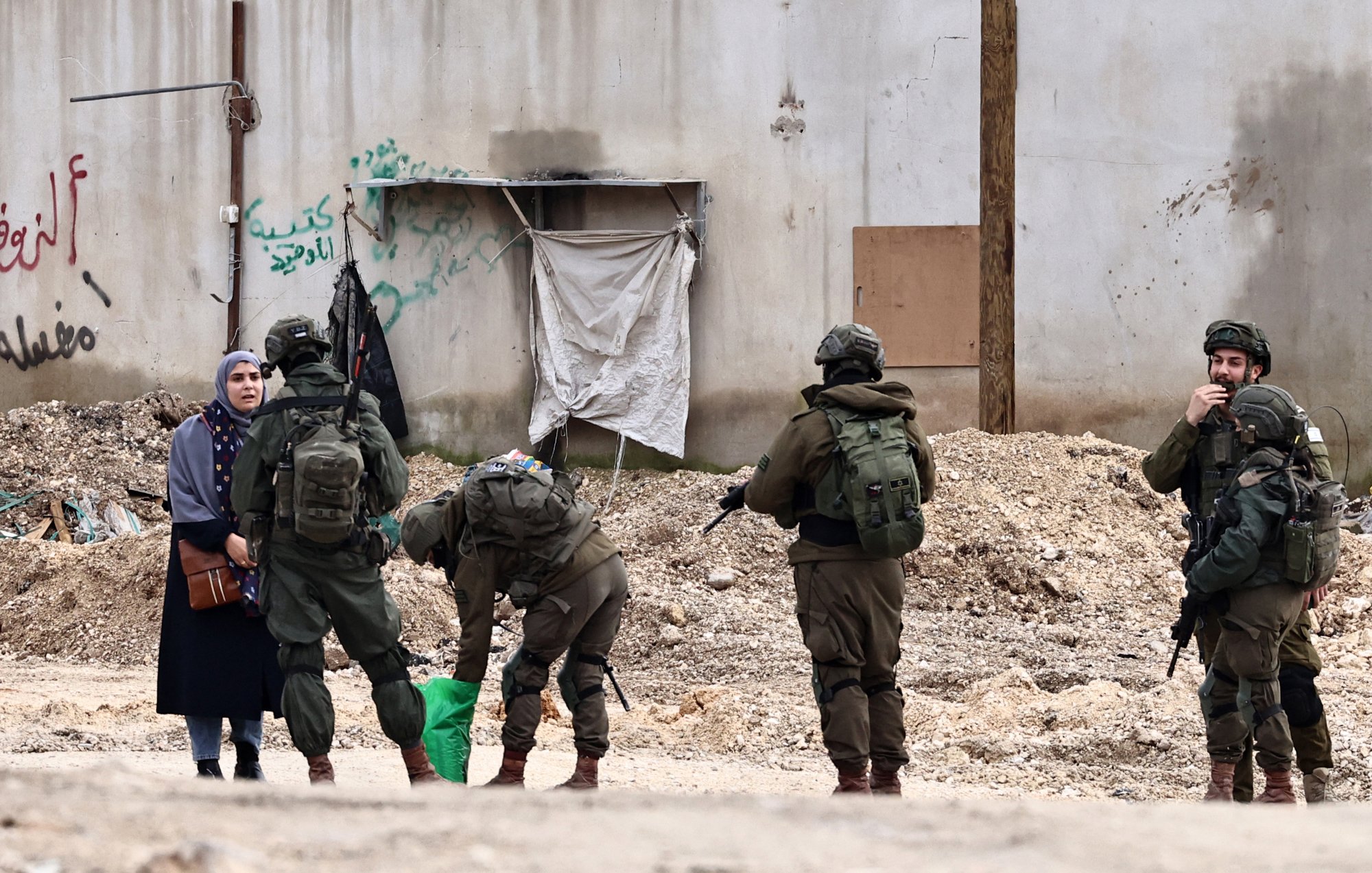 Soldiers in military gear interact with a woman in an urban setting, surrounded by debris.
