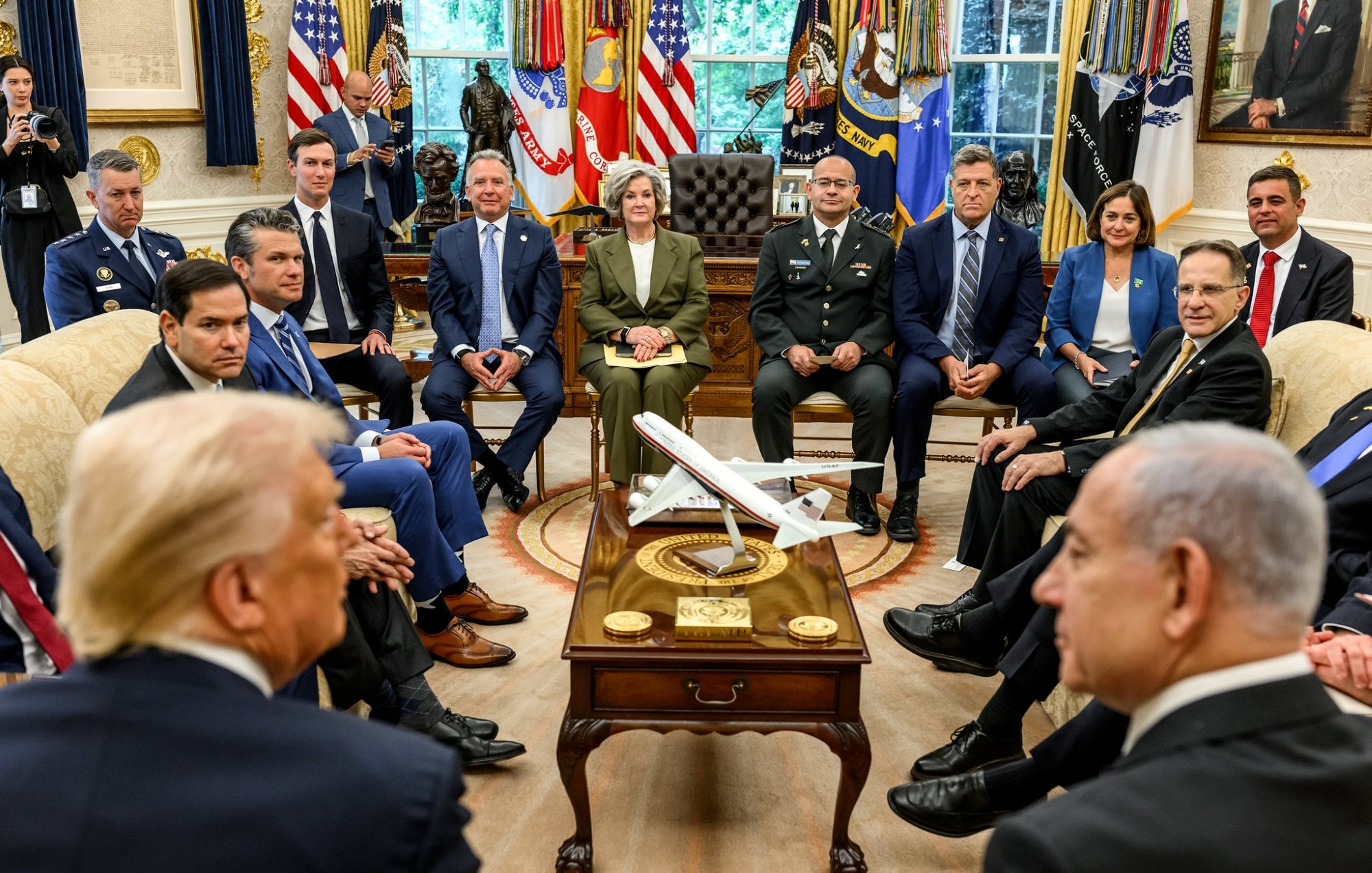 A formal meeting in the Oval Office with various officials and a model airplane on the table.