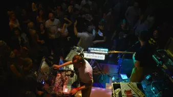 A lively concert scene with musicians using electronic instruments, surrounded by an energetic crowd.