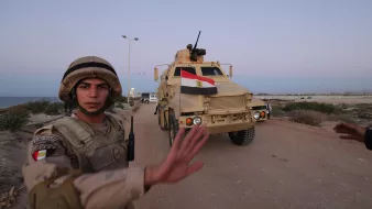 A soldier in uniform gestures as an armored vehicle marked with the Egyptian flag approaches.