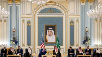 A formal meeting with leaders seated in an ornate room, a large portrait on the wall.