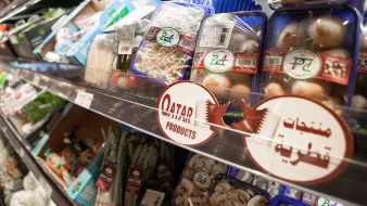 The image shows a grocery store shelf displaying a variety of packaged food items, primarily focused on fresh produce and seafood. There are containers of different types of mushrooms, noodles, and possibly other vegetables. A prominent sign labeled "Qatar Products" indicates a selection of items that are local or regional. The shelves are organized, showcasing a well-stocked array of products.