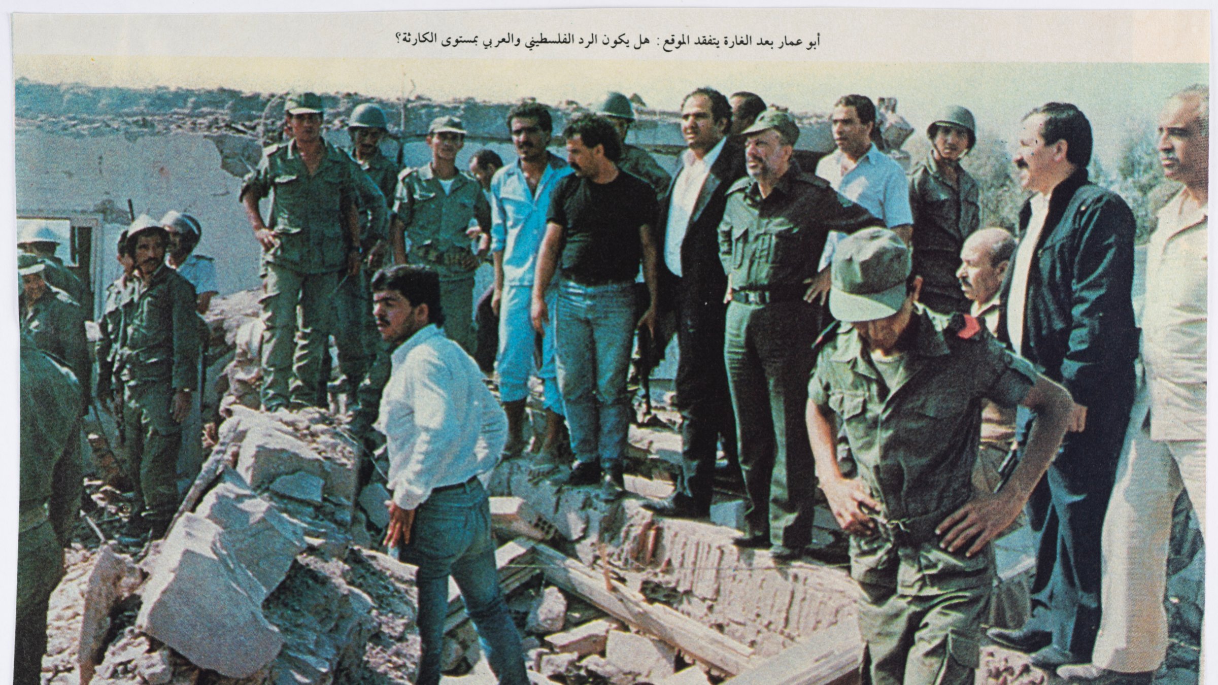 A group of military personnel and civilians gathers at a rubble site, surveying damage.