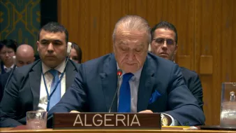 A man in a suit speaks at a podium labeled "Algeria" in a formal setting with delegates behind him.