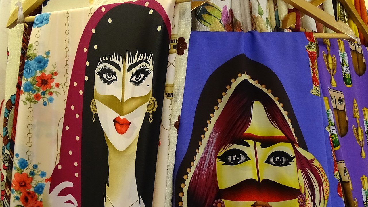 این تصویر شامل تصاویری از دو زن است که در طرحهای رنگارنگ و با جزئیات جذاب روی پارچهها نقاشی شدهاند. هر دو زن دارای ویژگیهای خاصی هستند، از جمله حالتهای صورت و پوشش متفاوت. طراحیها شامل رنگهای زنده و الگوهای متنوعی هستند که توجه را جلب میکنند. یکی از زنان به رنگهای تیره و دیگری به رنگهای روشنتر نمایش داده شده است که کنارههای شال یا دستمالی روی سر دارند. این نوع طراحیها معمولا در فرهنگهای مختلف به منظور نمایش زیبایی و سنتها استفاده میشود.