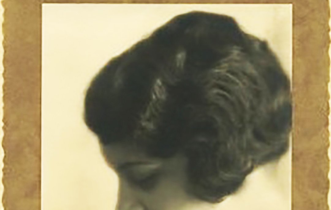 این تصویر یک پرتره سیاه و سفید از یک زن را نشان میدهد که در حالت آرام و تفکری به سمت راست نگاه میکند. موهای کوتاه و موجدار او به خوبی دیده میشود و نور به آرامی بر روی چهرهاش میتابد. زمینه تصویر نرم و محو است که بهطور کامل توجه را به چهره زن متمرکز میکند. حاشیهی تصویر حاشیهای زرد رنگ دارد که به زیبایی آن افزوده است.