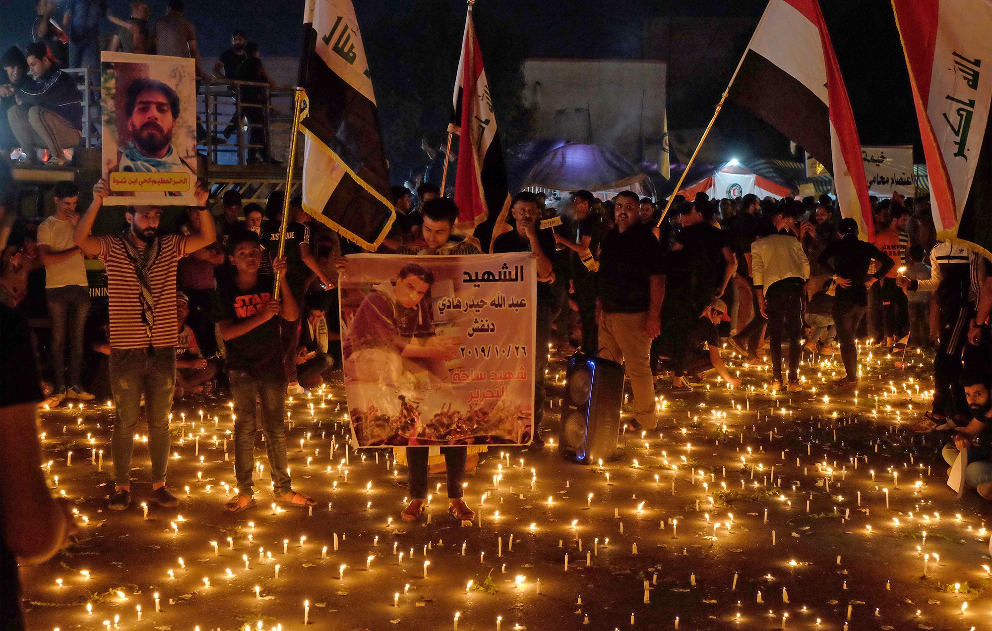 در این تصویر، جمعیتی از مردم در یک مکان بیرونی گرد هم آمدهاند، در حال برگزاری مراسمی با شمعهایی روشن. برخی از افراد پرچمهایی در دست دارند که به نظر میرسد نمایانگر گروههای مختلفی باشد. تعدادی از شرکتکنندگان همچنین پوسترهایی را حمل میکنند که تصاویری از افراد را نشان میدهد. نور شمعها فضای مراسم را روحانی و احساسی کرده و برجستگی آنها در تاریکی شب قابل توجه است. این تجمع ممکن است به منظور یادبود یا گرامیداشت افرادی خاص باشد.