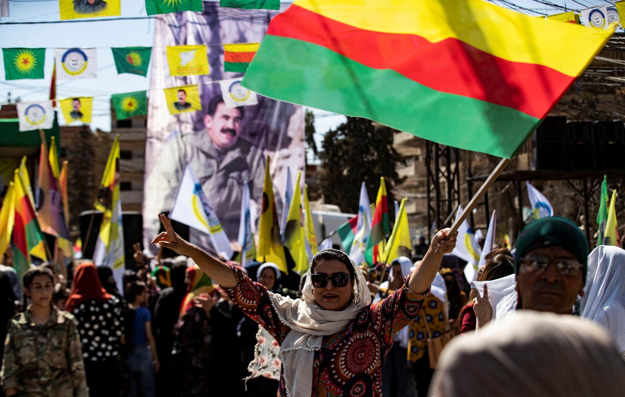 مردم در حال جشن و تظاهرات هستند، پرچمهای رنگی در دست دارند و شور و شوق به وضوح حس میشود.