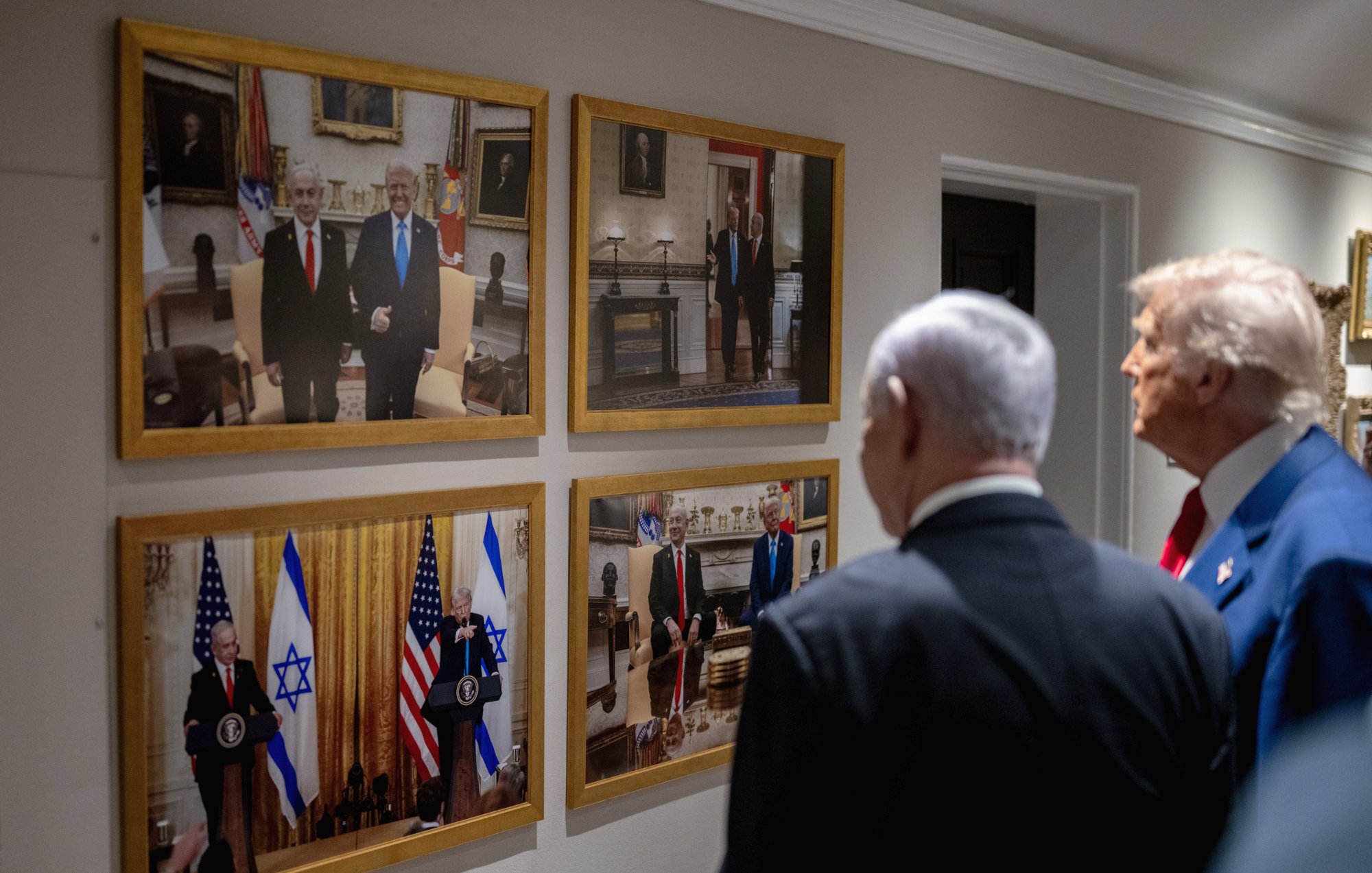 دو مرد در کت و شلوار در کنار یکدیگر ایستادهاند. تصاویر آنها بر دیواری قاب شدهاند.