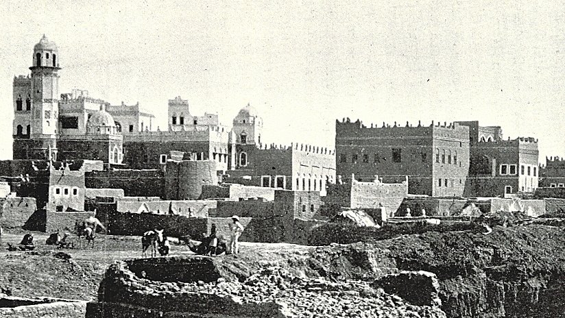 این تصویر نشاندهندهی یک منطقه تاریخی است که در آن ساختمانهای قدیمی با معماری سنتی دیده میشوند. در پسزمینه، چندین ساختمان با سقفهای گنبدی و تزئینات خاص وجود دارد. همچنین افرادی در حال کار در زمینهای جلویی دیده میشوند که ممکن است مشغول کشاورزی یا ساختوساز باشند. این صحنه، حال و هوای زندگی روزمره و تاریخی را در یک جامعه قدیمی به تصویر میکشد.