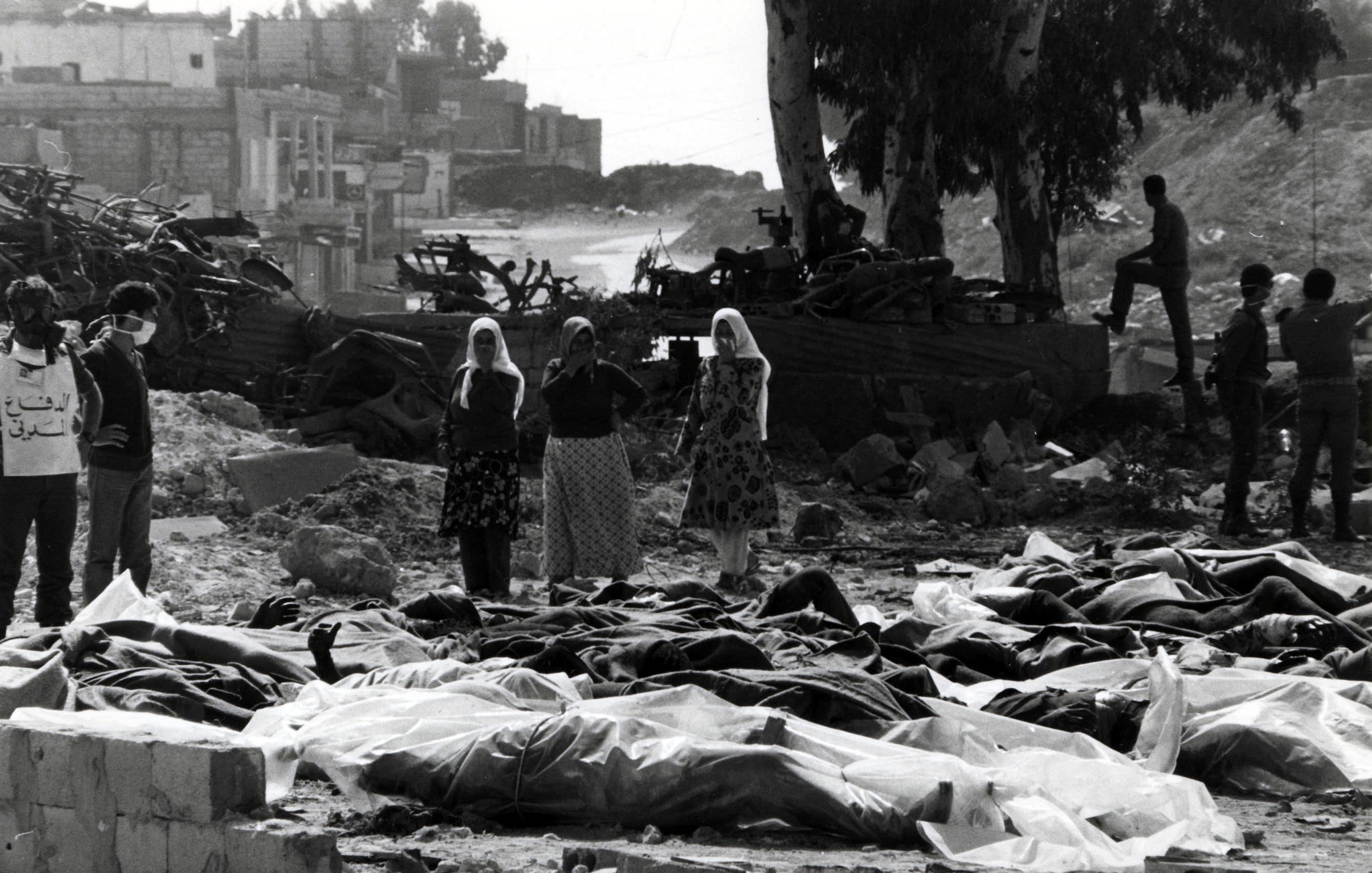 این تصویر نمایی غمانگیز و دلخراش از یک صحنهٔ بعد از بحران یا جنگ است. در جلوی تصویر، چندین جسد که با پارچهای پوشیده شدهاند، قرار دارند. در پسزمینه، گروهی از افراد حاضرند که به این صحنه نگاه میکنند، برخی از آنها اقدام به پوشاندن دهان و بینی خود کردهاند. درختان و ساختمانهای ویرانه در پشت زمینه به چشم میخورند، که حاکی از تخریب و ویرانی است. جو کلی تصویر شعاری از درد و مصیبت را منتقل میکند.