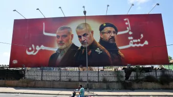 این تصویر یک بیلبورد بزرگ را نشان میدهد که سه نفر را به تصویر کشیده است. پسزمینه بیلبورد به رنگ قرمز است و ظاهراً به یک موضوع ملی یا سیاسی اشاره دارد. افراد تصویر شده به صورت نیمهتنه و با چهرههای جدی نمایش داده شدهاند. در پایین تصویر، یک موتور سوار در حال عبور است که نشاندهنده فعالیتهای روزمره در خیابان است. این بیلبورد ممکن است به یک رویداد خاص یا وحدت اشاره داشته باشد.