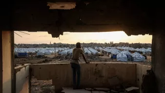 پسری از لبهی یک ساختمان ویران به سمت اردوگاه چادرها در غروب نگاه میکند.