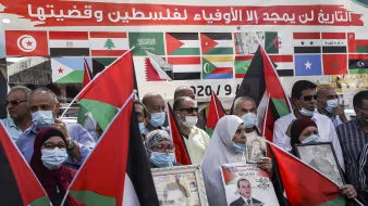 در این تصویر، گروهی از مردم در حال برگزاری یک تجمع هستند. آنها پرچمهای فلسطین را در دست دارند و برخی از آنها عکسهایی از شخصیتهای مهم را حمل میکنند. بر روی پسزمینه، پرچمهای کشورهای مختلف دیده میشود که نشان از حمایتهای بینالمللی از قضیه فلسطین دارد. همچنین، بسیاری از شرکتکنندگان دارای ماسک هستند، که ممکن است به دلیل رعایت مسائل بهداشتی باشد. احساس همبستگی و حمایت از آرمان فلسطین در چهرههای آنها نمایان است.