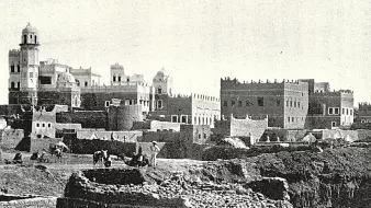 این تصویر نشاندهندهی یک منطقه تاریخی است که در آن ساختمانهای قدیمی با معماری سنتی دیده میشوند. در پسزمینه، چندین ساختمان با سقفهای گنبدی و تزئینات خاص وجود دارد. همچنین افرادی در حال کار در زمینهای جلویی دیده میشوند که ممکن است مشغول کشاورزی یا ساختوساز باشند. این صحنه، حال و هوای زندگی روزمره و تاریخی را در یک جامعه قدیمی به تصویر میکشد.