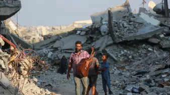 تصویر یک مرد را نمایش میدهد که در حال حرکت در میان ویرانههای یک منطقه تخریبشده است. او یک گیتار به دوش دارد و به نظر میرسد در حال نواختن یا آماده نواختن موسیقی باشد. دو کودک نیز به او نزدیک هستند، یکی از آنها به مرد وابسته است و به نظر میرسد او را دنبال میکند. در پسزمینه، آوار و خرابههای ساختمانها دیده میشود که نشانهای از یک بحران یا جنگ را نشان میدهد. نورخورشید در آسمان دیده میشود که ممکن است تصاویری از امید را القا کند.