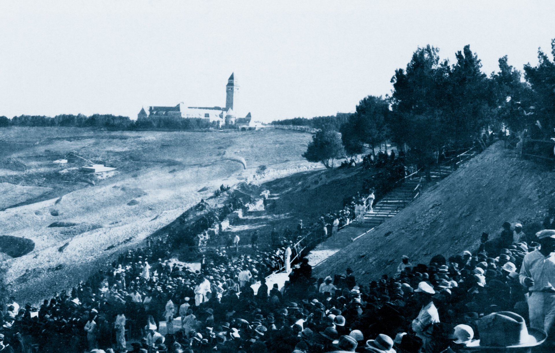 Une foule en bas d'une colline, avec un bâtiment en arrière-plan, scène historique.