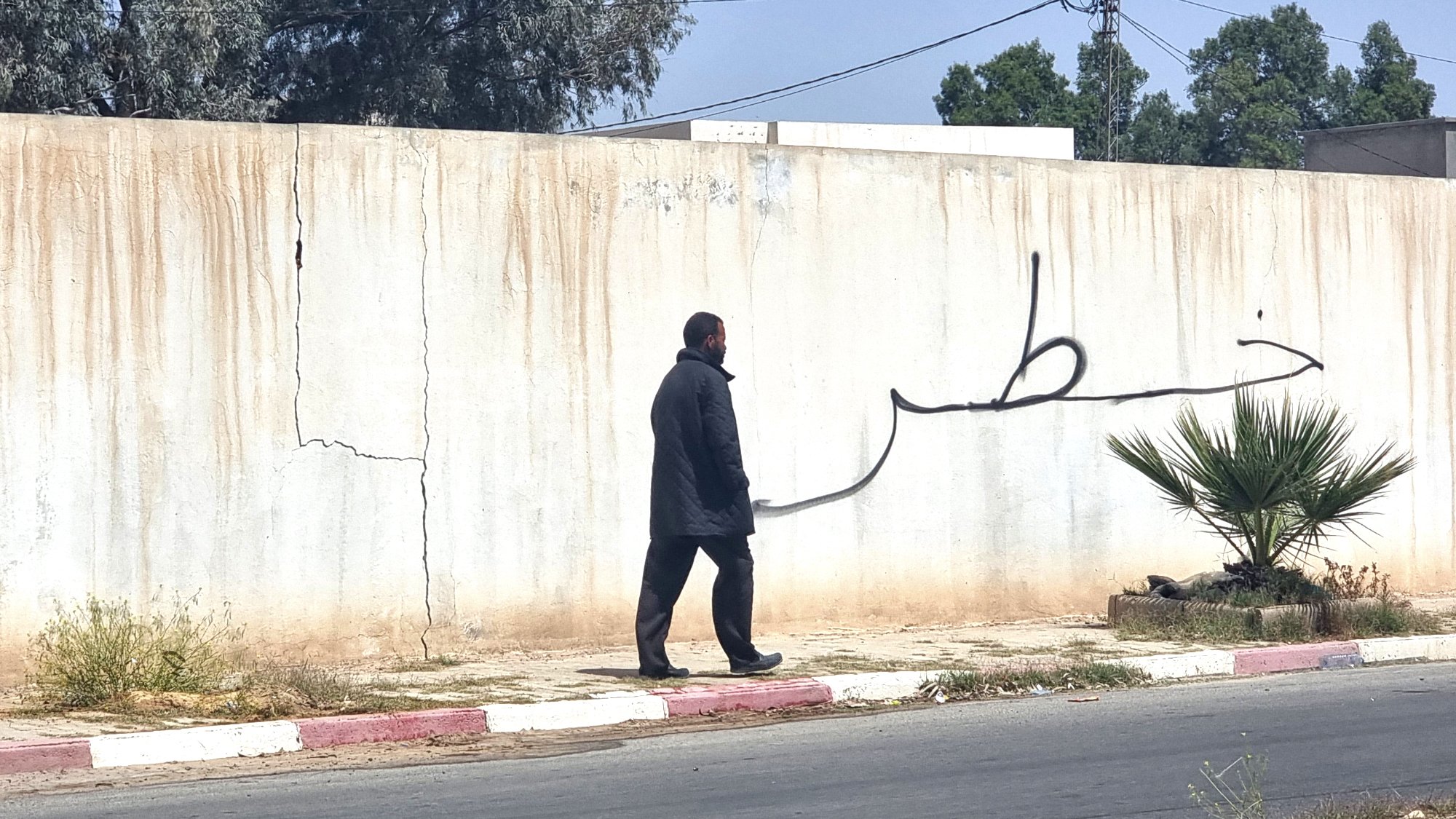 Un homme marche le long d'un mur avec une grande inscription en arabe.