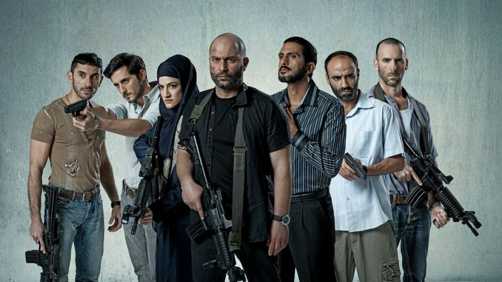 L'image montre un groupe de sept personnes armées, se tenant debout sur un fond gris. Ils ont des expressions déterminées et semblent en position de confrontation. Certains d'entre eux tiennent des armes à feu, tandis qu'une femme porte un hijab et se tient au milieu du groupe. Les hommes sont vêtus de vêtements variés, allant de casual à militaire. L'atmosphère est intense et pourrait suggérer un contexte d'action ou de tension.