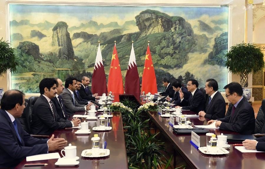 L'image montre une réunion formelle dans une salle de conférence. On peut y voir plusieurs personnes assises autour d'une longue table. À l'arrière-plan, il y a deux drapeaux, celui du Qatar et celui de la Chine, ainsi qu'une grande fresque représentant des montagnes et des paysages. Les participants semblent engagés dans une discussion, avec des tasses et des documents disposés sur la table. L'ambiance semble sérieuse et professionnelle, indiquant un dialogue diplomatique entre les deux pays.