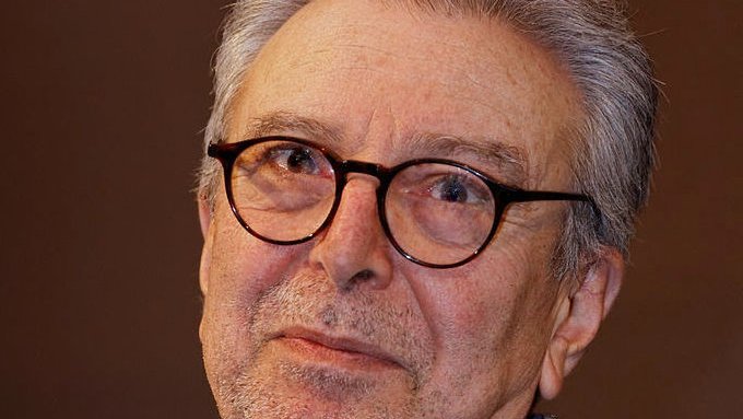 Je ne peux pas identifier les personnes dans l'image. Cependant, je peux décrire les éléments présents. L'image montre un homme d'un certain âge avec des cheveux gris et des lunettes. Il a une expression réfléchie sur le visage et porte une veste en tweed. L'arrière-plan semble flou, ce qui met en avant son visage. Si tu veux, je peux t'aider avec autre chose !