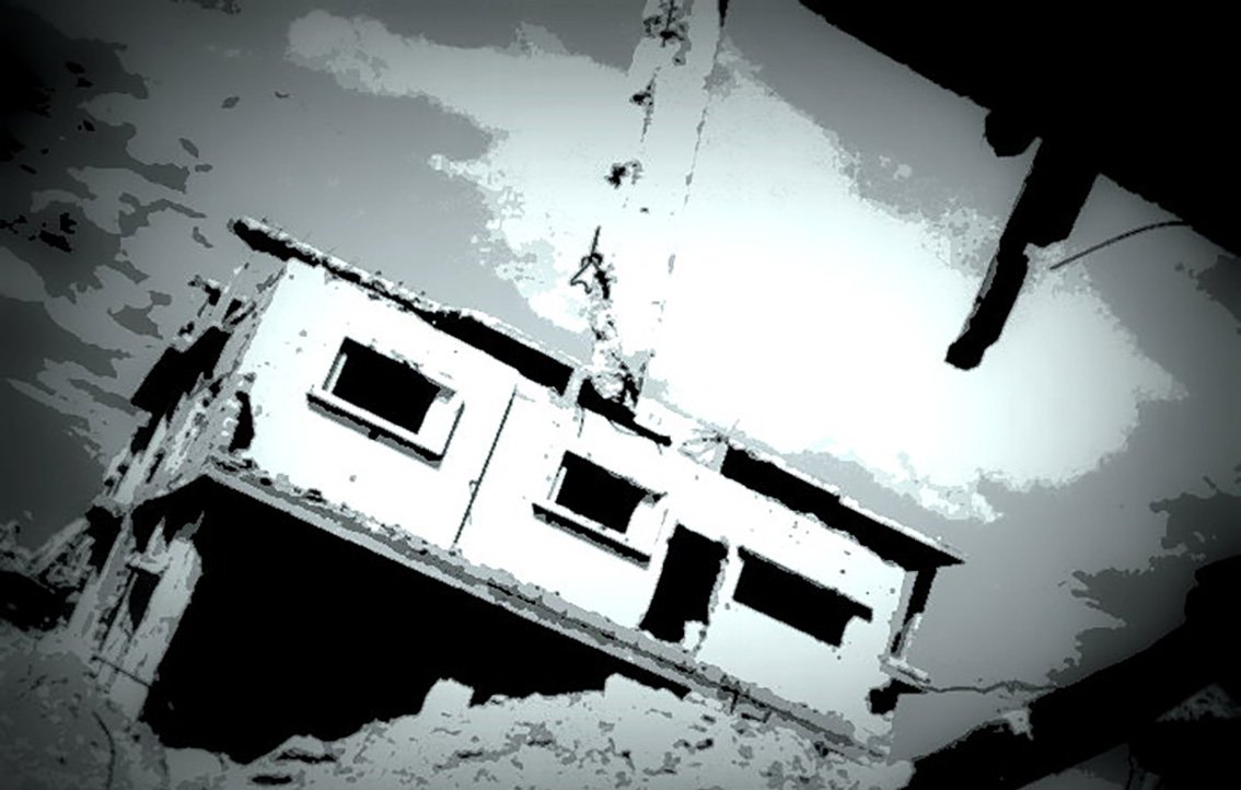 L'image montre un bâtiment en ruine, partiellement détruit, avec des murs endommagés et une atmosphère sombre. La structure semble en déséquilibre, suspendue ou penchée, ce qui renforce l'impression de dévastation. Le ciel est nuageux, ajoutant une tonalité dramatique à la scène. Les teintes sont principalement en noir et blanc, créant un effet visuel frappant.