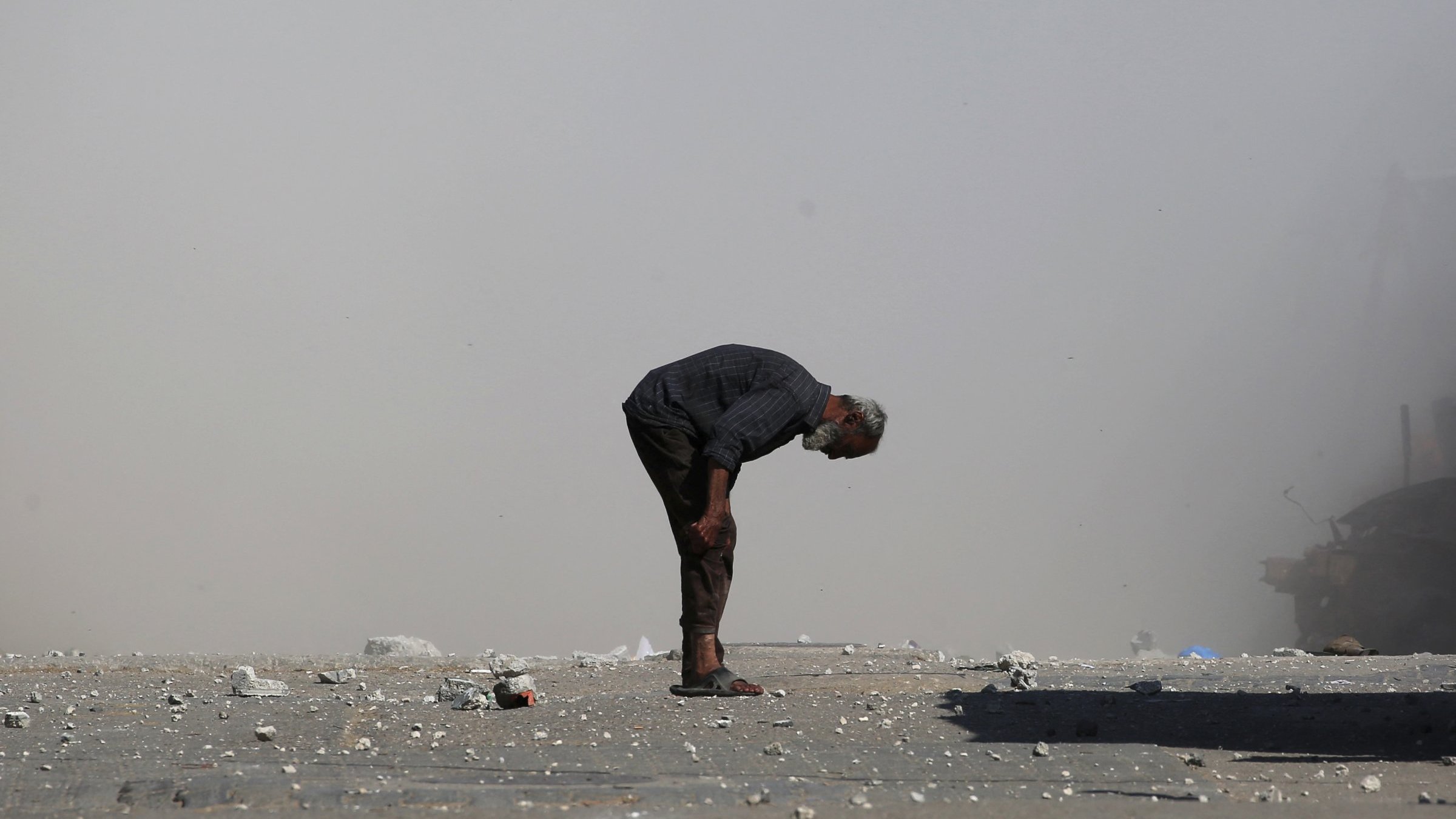 Un homme âgé se penche, entouré de débris et de poussière.