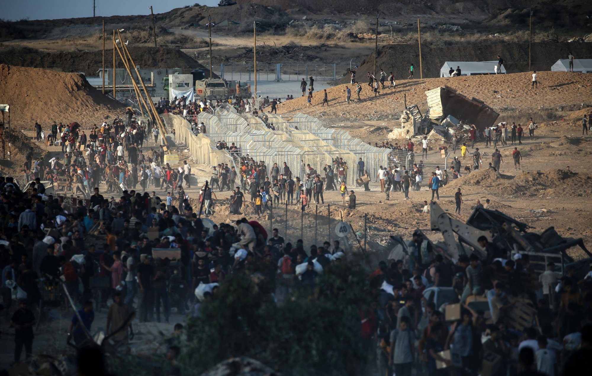 Une foule se rassemble près de clôtures dans un paysage aride et dévasté.