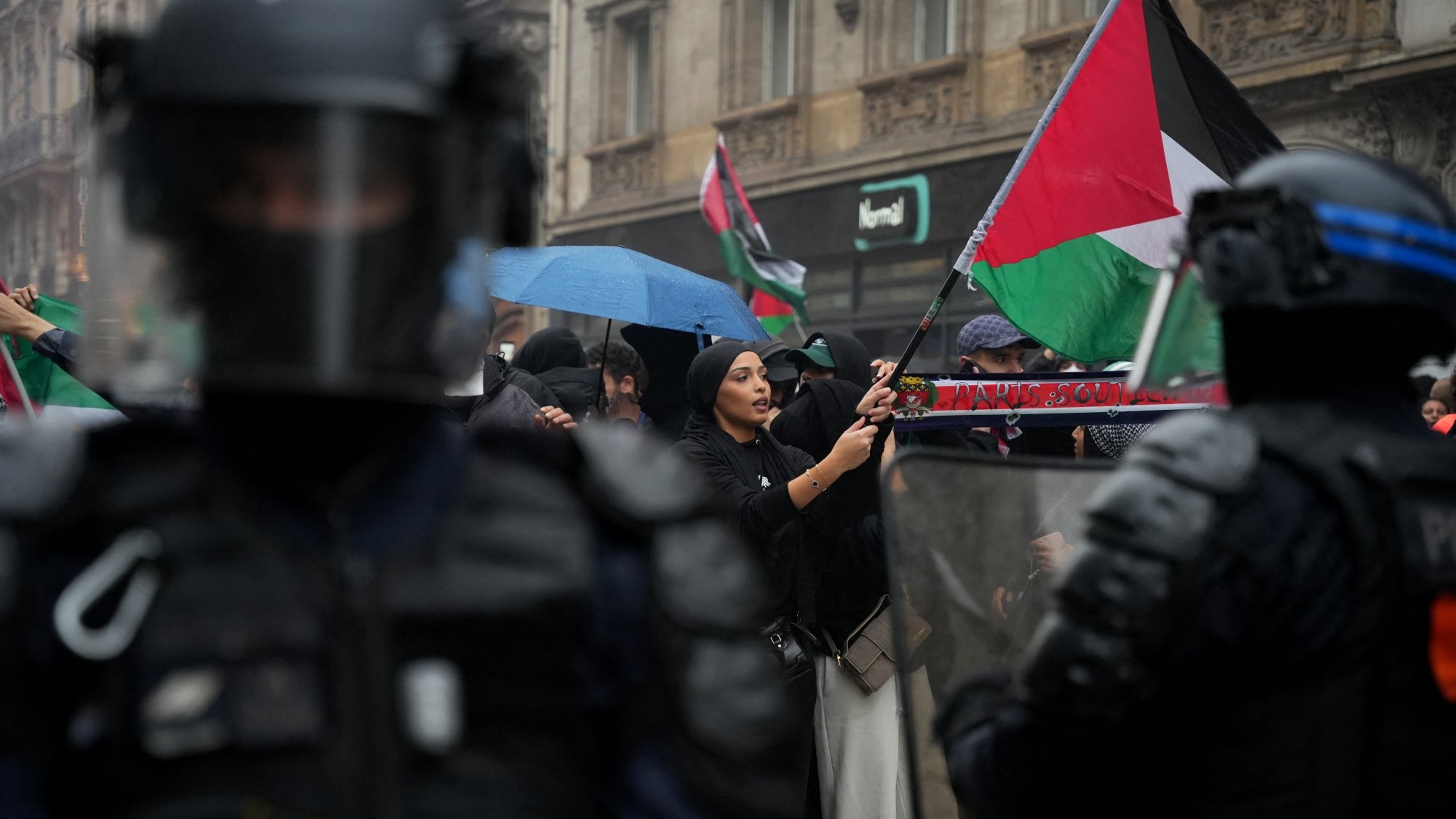 Manifestation avec des drapeaux palestiniens, policiers en tenue anti-émeute, ambiance tendue.