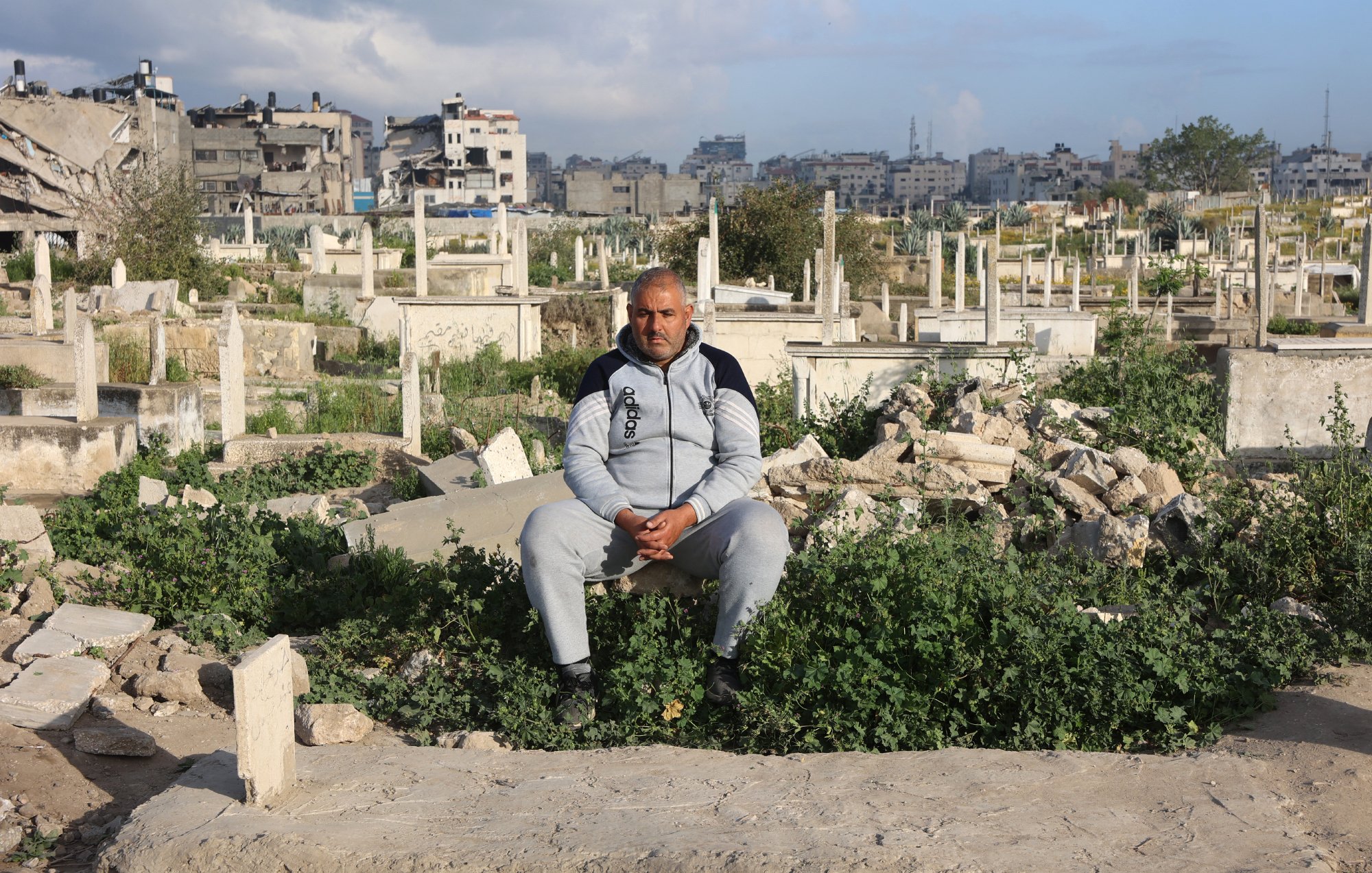 Un homme assis parmi des tombes dans un cimetière, entouré de végétation.